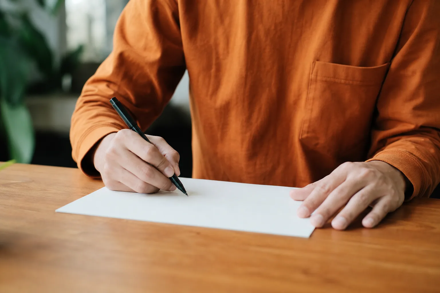 person in orange long sleeve shirt writing on white paper