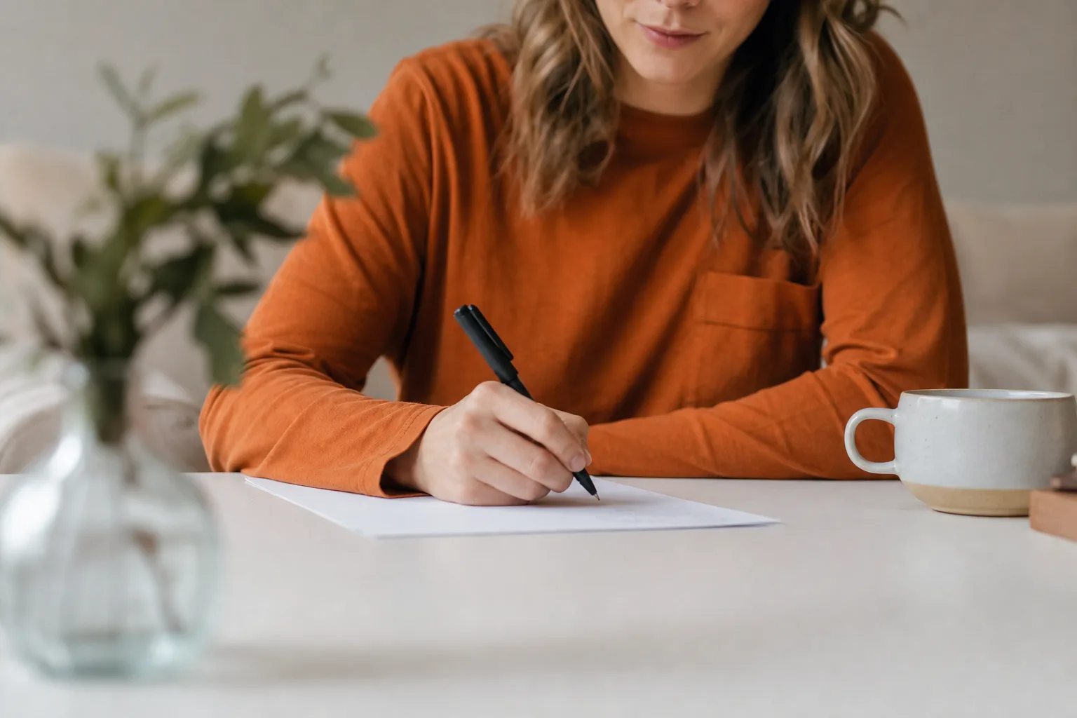person in orange long sleeve shirt writing on white paper